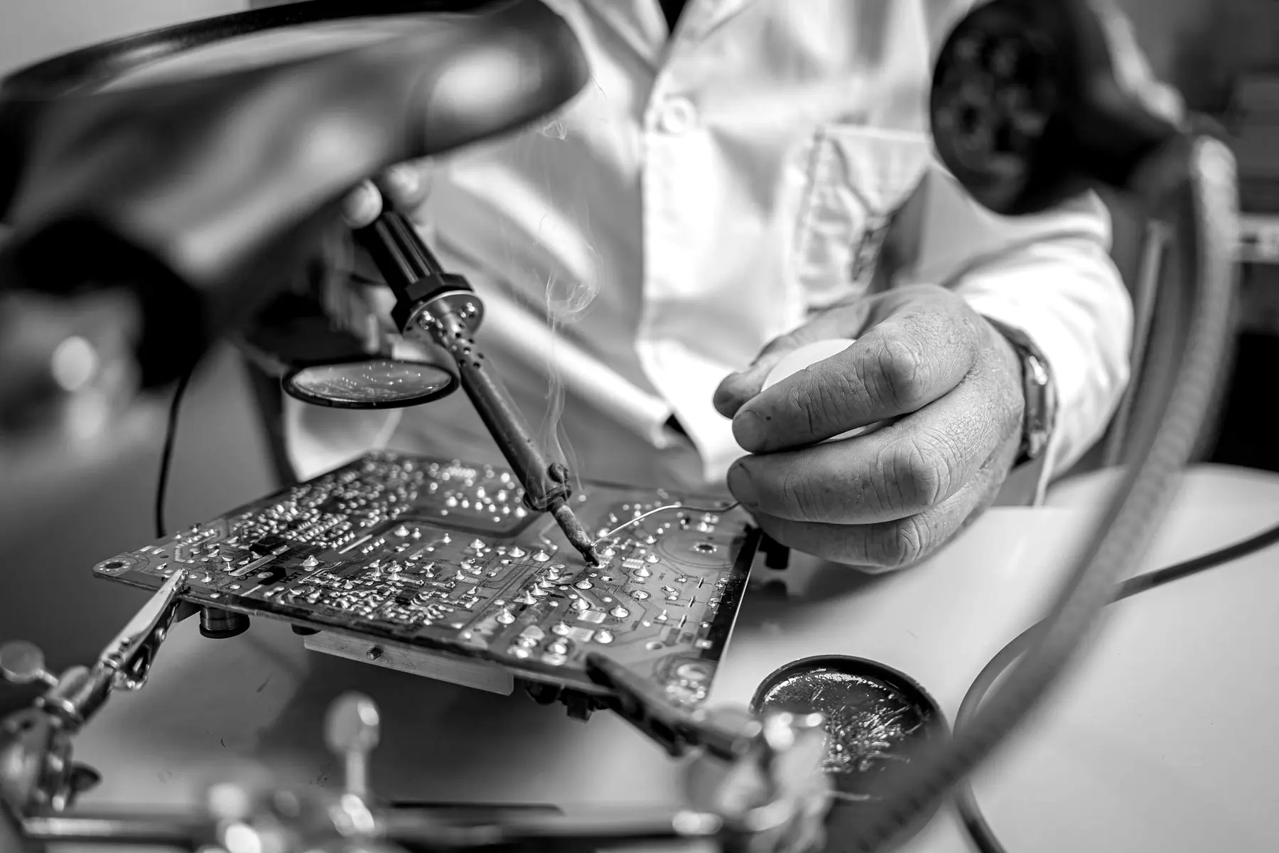 A technician soldering a green circuit board under a magnifier