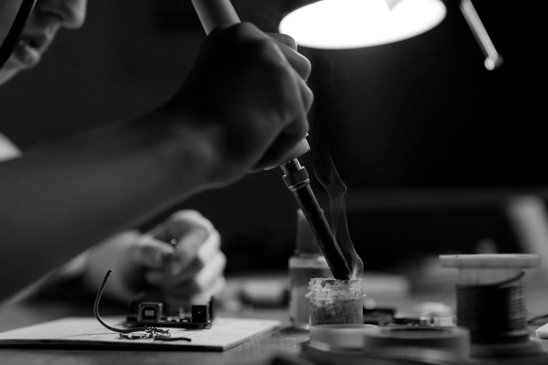 Hands soldering a prototype board under a desk lamp