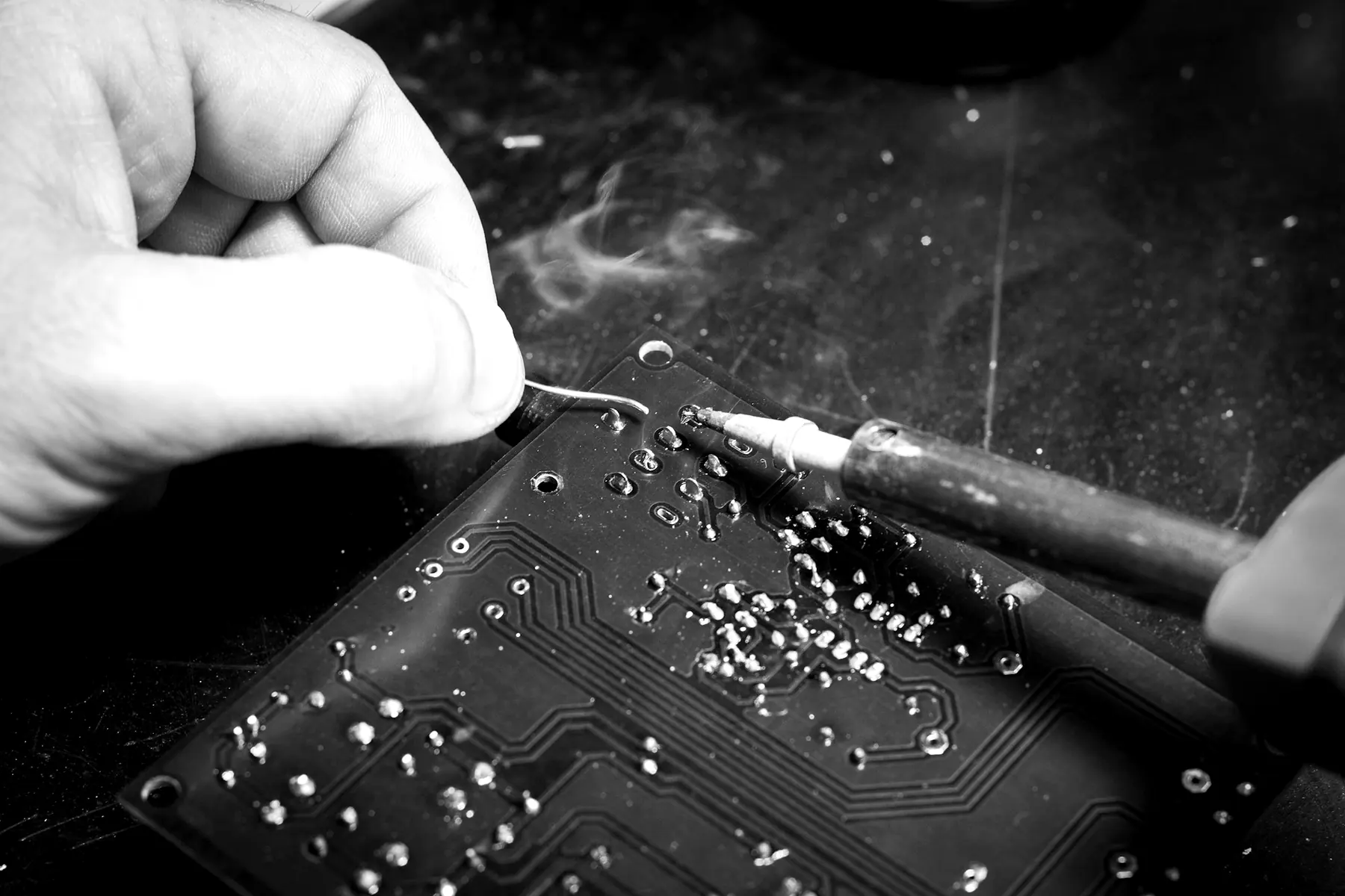 A hand soldering a joint on a black circuit board, with flux smoke rising